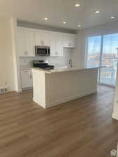 Kitchen featuring light countertops, visible vents, appliances with stainless steel finishes, white cabinets, and an island with sink