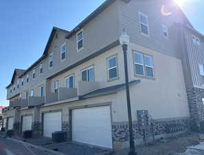 Exterior space with a garage, central air condition unit, and stucco siding