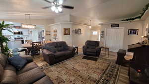 Living area featuring a ceiling fan, lofted ceiling, baseboards, and wood finished floors