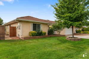 Single story home featuring driveway, a garage, a tiled roof, a front lawn, and stucco siding