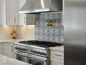 Kitchen with light stone counters, white cabinets, double oven range, beautiful  tiled backsplash, and ventilation hood