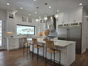 Kitchen with white cabinets, appliances with stainless steel finishes, glass insert cabinets, a center island, and wall chimney range hood