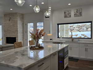 Kitchen featuring light stone counters, white cabinets, a sink, and decorative light fixtures