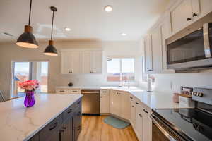 Kitchen with white cabinetry, stainless steel appliances, a sink, and decorative light fixtures