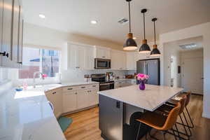 Kitchen featuring light stone countertops, visible vents, appliances with stainless steel finishes, and white cabinets