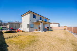 Back of property featuring a lawn, a patio, a fenced backyard, a trampoline, and stucco siding