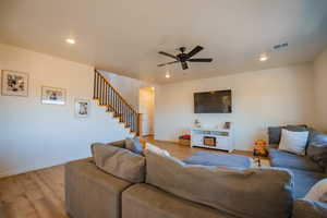 Living room with light wood-style flooring, visible vents, stairway, and recessed lighting