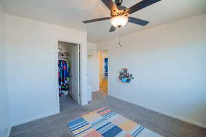 Unfurnished bedroom featuring light carpet, a ceiling fan, baseboards, a closet, and a walk in closet