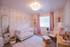 Carpeted bedroom featuring baseboards, a crib, visible vents, and wallpapered walls