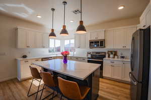 Kitchen featuring light stone counters, decorative light fixtures, stainless steel appliances, visible vents, and white cabinets