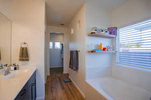 Bathroom featuring baseboards, visible vents, wood finished floors, a garden tub, and vanity