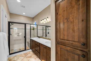 Full bath with double vanity, visible vents, tile patterned floors, a shower stall, and a sink