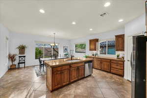 Kitchen featuring decorative light fixtures, visible vents, appliances with stainless steel finishes, a kitchen island with sink, and a sink