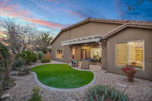 Back of house at dusk featuring fence, a yard, a tiled roof, stucco siding, and a patio area