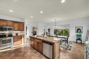 Kitchen featuring brown cabinets, stainless steel appliances, hanging light fixtures, a kitchen island with sink, and a sink