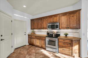 Kitchen featuring stone countertops, recessed lighting, appliances with stainless steel finishes, decorative backsplash, and brown cabinets