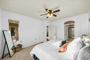 Bedroom with light carpet, baseboards, arched walkways, a ceiling fan, and ensuite bath