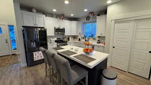 Kitchen featuring white cabinetry, appliances with stainless steel finishes, a center island, and wood-type flooring