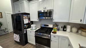 Kitchen with light stone counters, stainless steel appliances, light hardwood / wood-style floors, and white cabinets