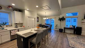 Kitchen featuring hanging light fixtures, stainless steel dishwasher, a kitchen breakfast bar, a kitchen island, and white cabinets