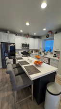 Kitchen featuring appliances with stainless steel finishes, white cabinetry, a kitchen breakfast bar, hardwood / wood-style flooring, and a center island