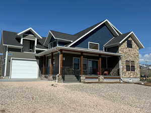 View of front of house with covered porch, stone siding, a shingled roof, and a garage