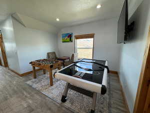 Rec room featuring lofted ceiling, a textured ceiling, wood finished floors, and baseboards