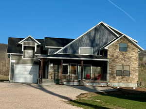 View of front of home featuring driveway, stone siding, an attached garage, covered porch