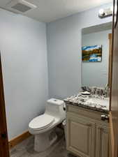 Half bathroom with toilet, wood finished floors, a textured ceiling, and vanity