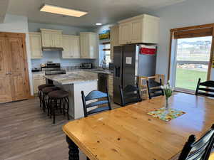 Kitchen featuring under cabinet range hood, a kitchen island, a sink, appliances with stainless steel finishes, and cream cabinetry