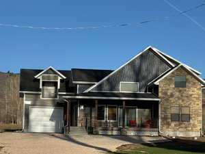 View of front of property with a garage, driveway, stone siding and a porch