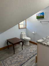 Bathroom with a textured ceiling, wood finished floors, toilet, and lofted ceiling