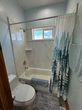 Full bath with shower / tub combo with curtain, toilet, and wood finished floors