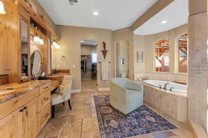 Bathroom with a garden tub, stone tile floors, visible vents, vanity, and baseboards