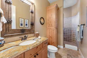 Bathroom with toilet, stone tile floors, vanity, baseboards, and walk in shower