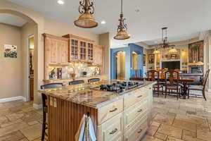 Kitchen featuring stainless steel gas cooktop, glass insert cabinets, a kitchen island, and stone tile flooring