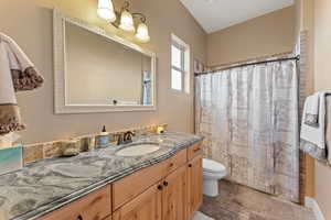 Full bathroom with toilet, a shower with curtain, stone tile flooring, and vanity