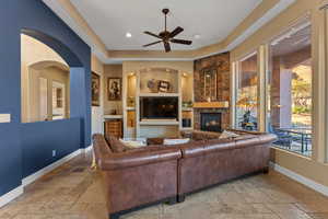 Living area featuring a ceiling fan, baseboards, a stone fireplace, and stone tile floors