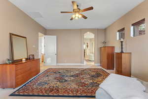 Bedroom featuring arched walkways, ceiling fan, visible vents, baseboards, and ensuite bath