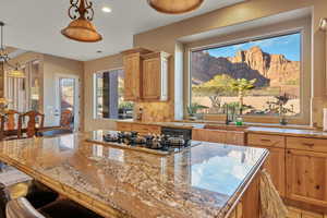 Kitchen featuring light stone counters, a kitchen breakfast bar, decorative light fixtures, stainless steel gas cooktop, and a sink