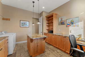 Kitchen featuring washing machine and dryer, a kitchen island, hanging light fixtures, open shelves, and stone tile flooring