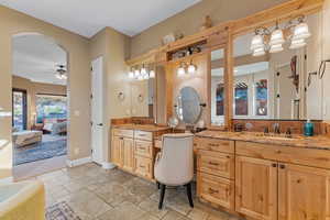 Ensuite bathroom with a sink, ensuite bath, stone tile flooring, and baseboards