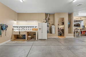 Garage featuring secured water heater, a workshop area, visible vents, white fridge with ice dispenser, and baseboards