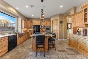 Kitchen with black appliances, light stone counters, stone tile floors, and a center island