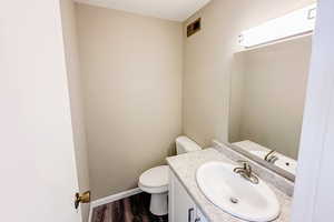 Half bath featuring visible vents, baseboards, toilet, wood finished floors, and vanity