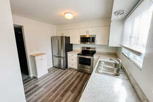 Kitchen with baseboards, white cabinets, appliances with stainless steel finishes, dark wood-style flooring, and a sink