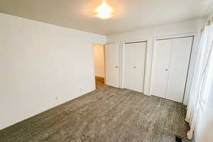 Unfurnished bedroom with carpet, visible vents, and two closets