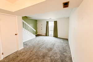 Carpeted empty room with stairway, visible vents, and baseboards