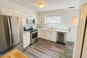 Kitchen with white cabinets, appliances with stainless steel finishes, light countertops, and a sink