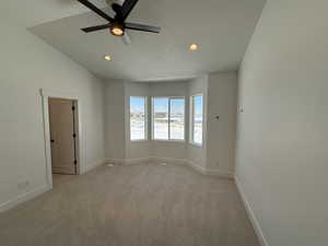 Empty room with a textured ceiling, ceiling fan, light colored carpet, baseboards, and vaulted ceiling